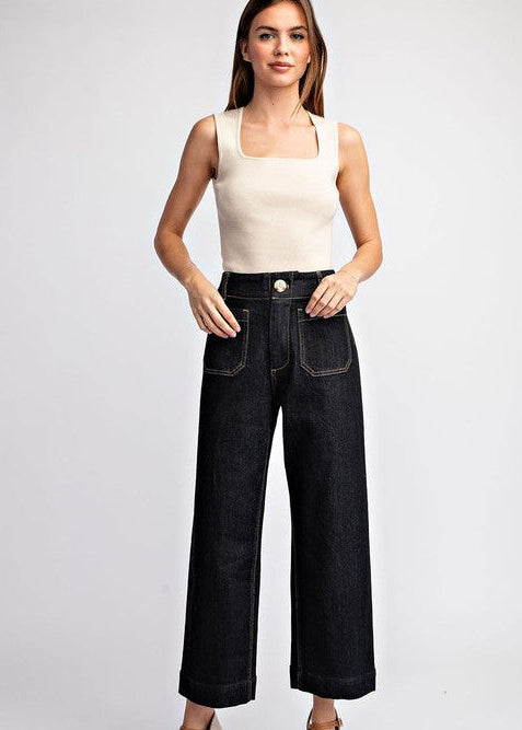 Woman wearing a beige tank top and black wide-leg jeans on a white background